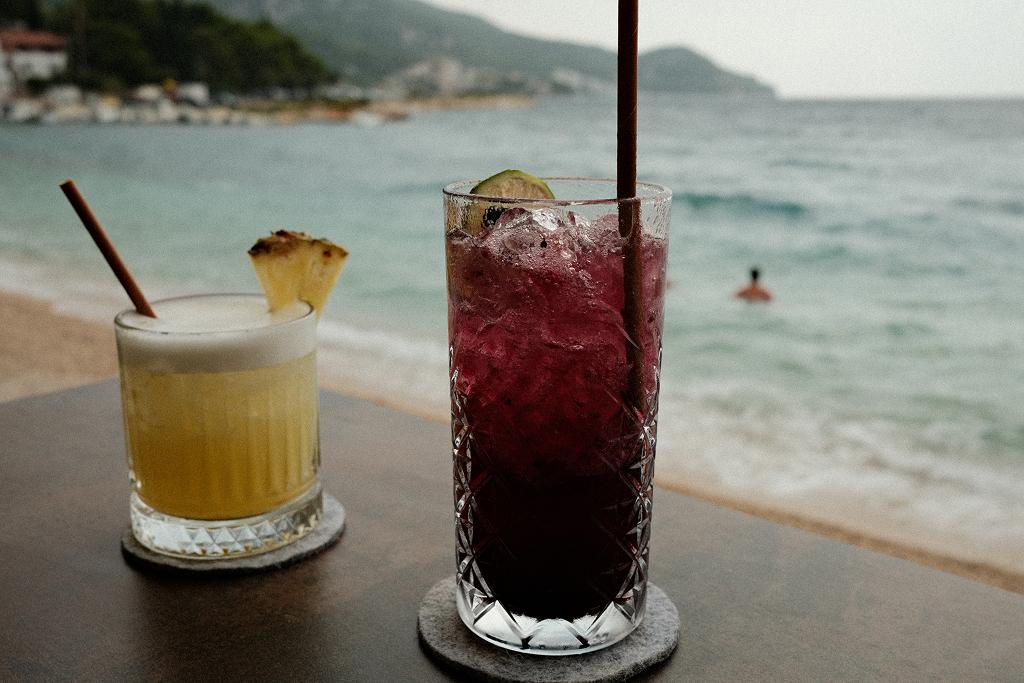 Two cocktails on a table by the sea, with a swimmer in the water behind